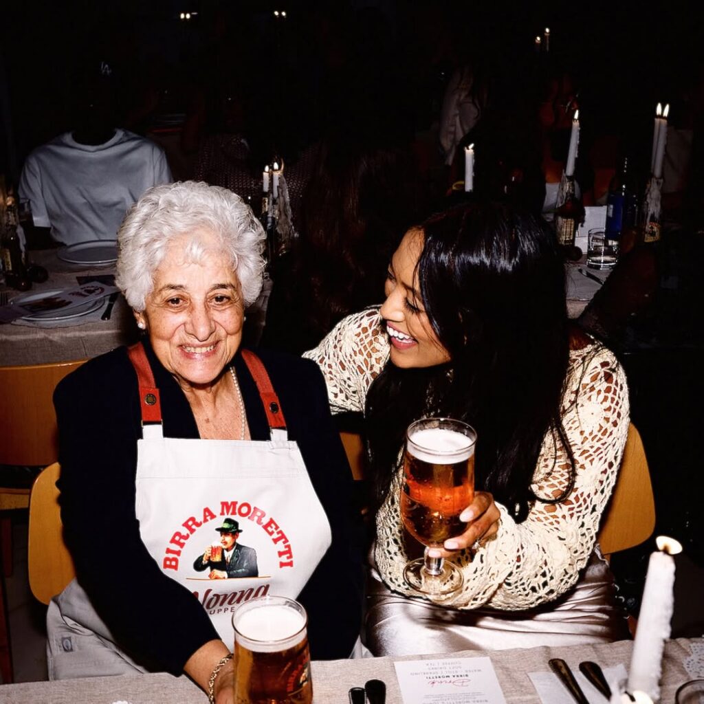 A nonna from the club smiles at the camera while a fan looks at her.