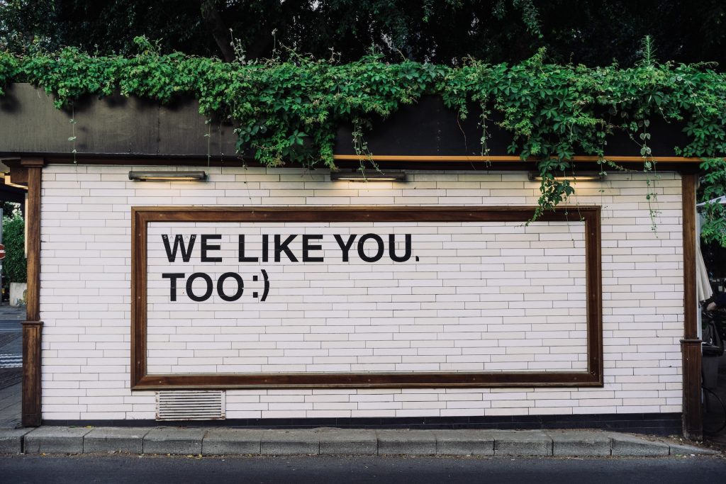 "We like you too" with smile emoji on white brick wall